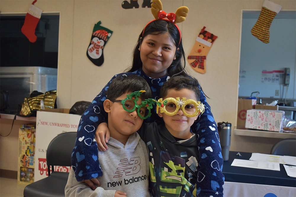Children smiling in festive holiday glasses and reindeer ears